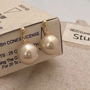Macro detail of large cream pearl earrings with gold spherical studs on a vintage box