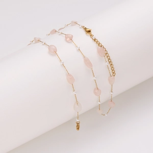 Gold chain necklace with pink irregular gemstones and pearls on white pedestal