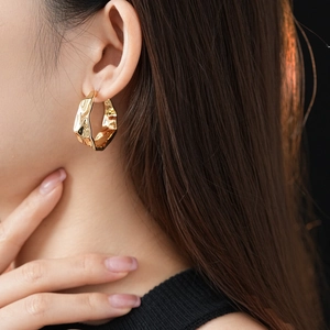 Close-up of golden C-shaped hoop earring with irregular wrinkled texture on a model's ear