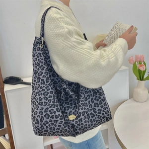 Detailed close-up of leopard print canvas tote bag with gold logo plaque on corduroy texture
