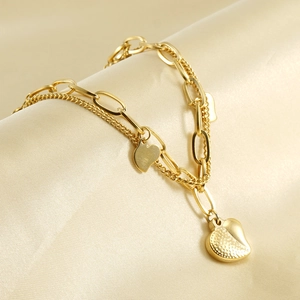 Macro view of gold-plated double-layer bracelet with textured heart charms on beige silk