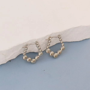 Detailed macro view of silver beaded hoop earrings on a textured stone display
