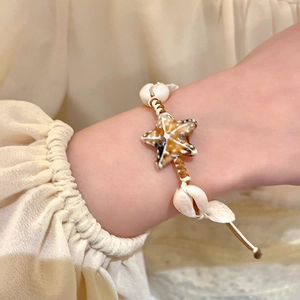 Detail of seashell and starfish bracelet on wrist with woven cord for beach vacation style