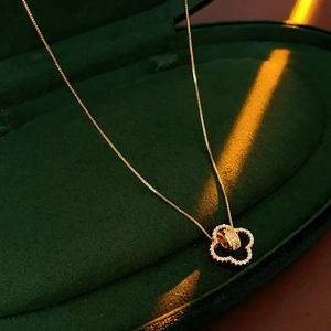 Macro view of 18K gold-plated clover pendant with inlaid zircons in a green velvet box