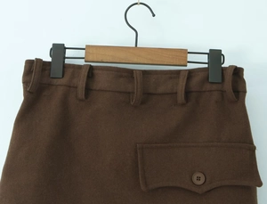 Détail de la jupe en laine marron avec poche à rabat boutonnée et passants à la taille