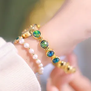 Luxury gold watch with peacock green gemstones and pearl bracelet on a woman's wrist