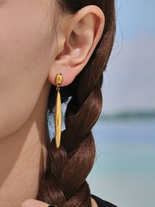 Detail of long gold teardrop earrings on model with high polish finish and ocean view