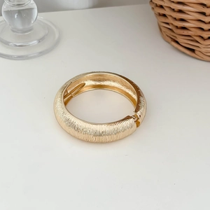 Detailed view of a golden open bangle featuring a unique textured wrinkled design