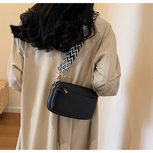 Detail of black crossbody bag featuring a geometric patterned wide strap and pebble texture