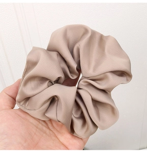 Close-up of a large satin scrunchie in khaki held by hand showing soft silk texture