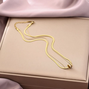 Detail of a golden double-layered snake chain necklace with a crystal cylinder pendant