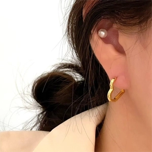 Close-up of minimalist heart-shaped gold earrings with pearl backs worn by a model