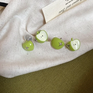 Detail of light green enamel apple earrings and ear clips on textured linen fabric