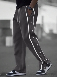 Detail of dark grey track pants featuring side double stripes and metal snap buttons