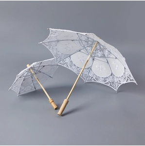Detailed embroidery on white lace bridal umbrellas with vintage wooden handles for weddings