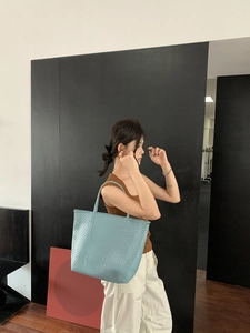 Light blue woven tote bag shown on shoulder of a model for a summer vacation look
