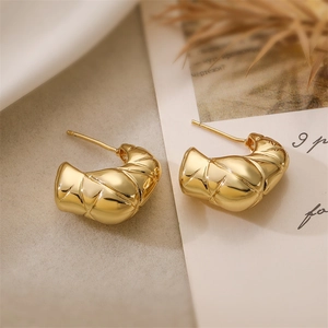Detailed view of golden textured heart studs with high-gloss finish on a minimal background
