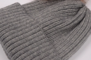 Détail du bonnet en maille grise avec texture côtelée et pompon en fausse fourrure