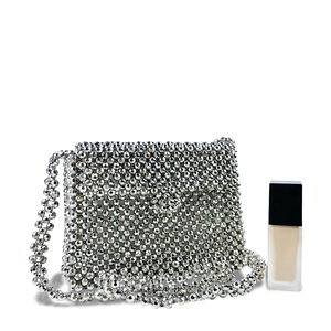 Detail of silver beaded crossbody bag with metallic beads beside a makeup bottle