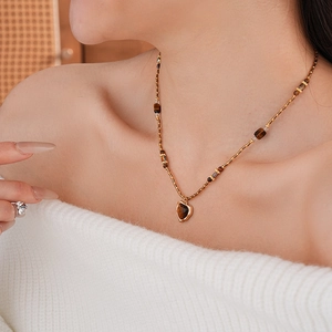 Détail d'un collier en perles marron avec pendentif cœur doré porté par un mannequin