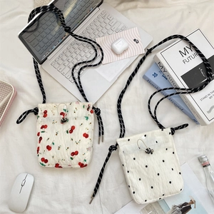 Detail of floral canvas crossbody bags with cherry patterns and rope straps on a desk