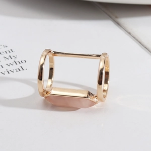 Detail of pink crystal stone set in a geometric gold double ring on a white surface