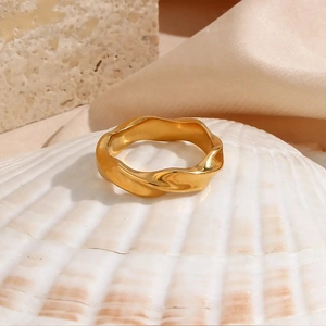 Detailed view of wave-shaped gold plated ring resting on a decorative shell