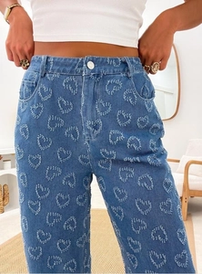 Detailed close-up of blue denim jeans featuring 3D heart-shaped floral texture and patterns