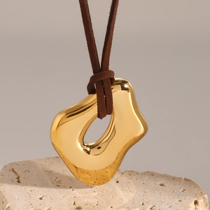 Polished gold irregular liquid metal pendant on brown suede cord over stone background