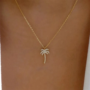 Close-up of a gold palm tree pendant necklace with white crystals on a woman neck