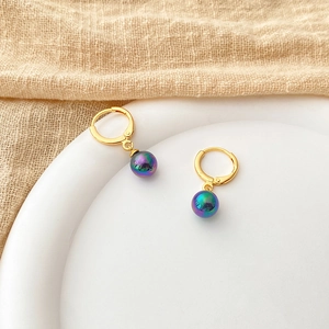 Detail of 18K gold-plated earrings featuring iridescent purple pearl charms on white tray