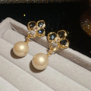 Macro detail of gold-plated clover earrings with clear crystals and champagne pearl drop