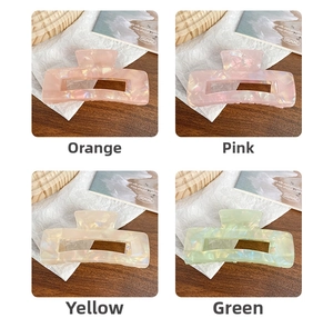 Detail of four colorful iridescent acetate hair claws in orange, pink, yellow, and green