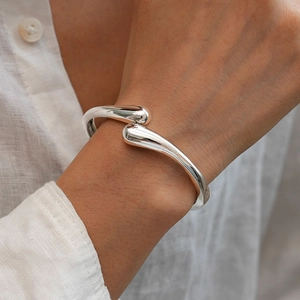 Close-up of polished silver teardrop cuff bracelet on a female wrist in minimalist style