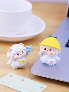 Close-up of cute mini sheep resin figurines on a desk near a laptop and coffee cup
