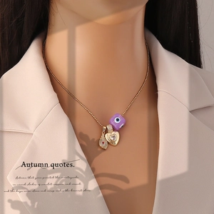 Close-up of golden beaded necklace with purple evil eye heart and feather charms on model