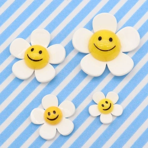 Detailed view of four white smiley face flower charms in three sizes on striped background