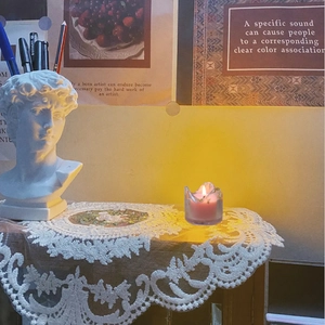 Rosa Duftkerze im Klarglas leuchtet auf einer romantischen Spitzentischdecke