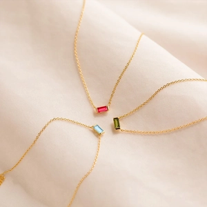 Detailed shot of gold necklaces with emerald, sapphire, and ruby baguette-cut crystals