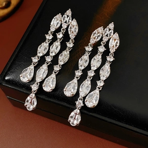 Macro detail of silver needle drop earrings with zircon teardrops on black leather