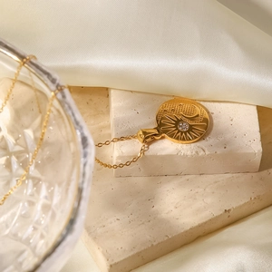 Detailed view of a gold sun and moon pendant necklace on a beige stone surface