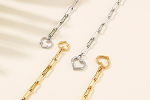 Close-up of gold and silver paperclip bracelets with hollow heart charms on beige backdrop