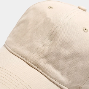 Detailed close-up of cotton twill fabric and stitching on a beige baseball cap