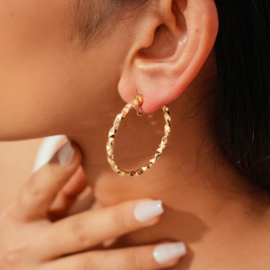 Detail shot of golden geometric twisted earrings featuring a 3D pyramid cut texture