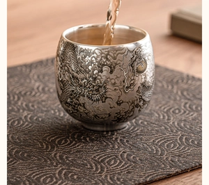 Gros plan du thé versé dans une tasse en argent avec un motif de dragon finement sculpté