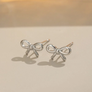 Close-up of elegant silver bow stud earrings in stainless steel on a beige surface