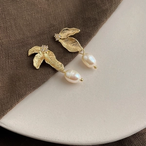 Detailed close-up of golden leaf earrings with white teardrop pearls on a ceramic dish