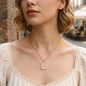 Close-up of gold tarot pendant with pink enamel and snake motif worn by a model