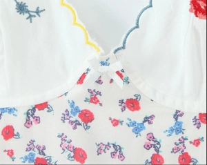 Détail du col en V d'une robe fleurie avec bordure brodée et petit noeud satiné