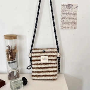Detail of plush striped crossbody bag with rope strap and woven label on white wall
